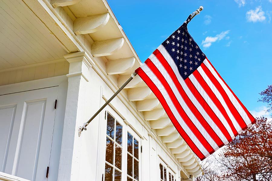 About Our Agency - American Flag Waving On the Front Porch of a White Home on a Sunny Day