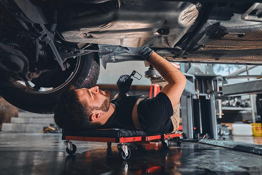 Business Insurance - Young Mechanic Working On the Underside of a Car, Wearing Overalls